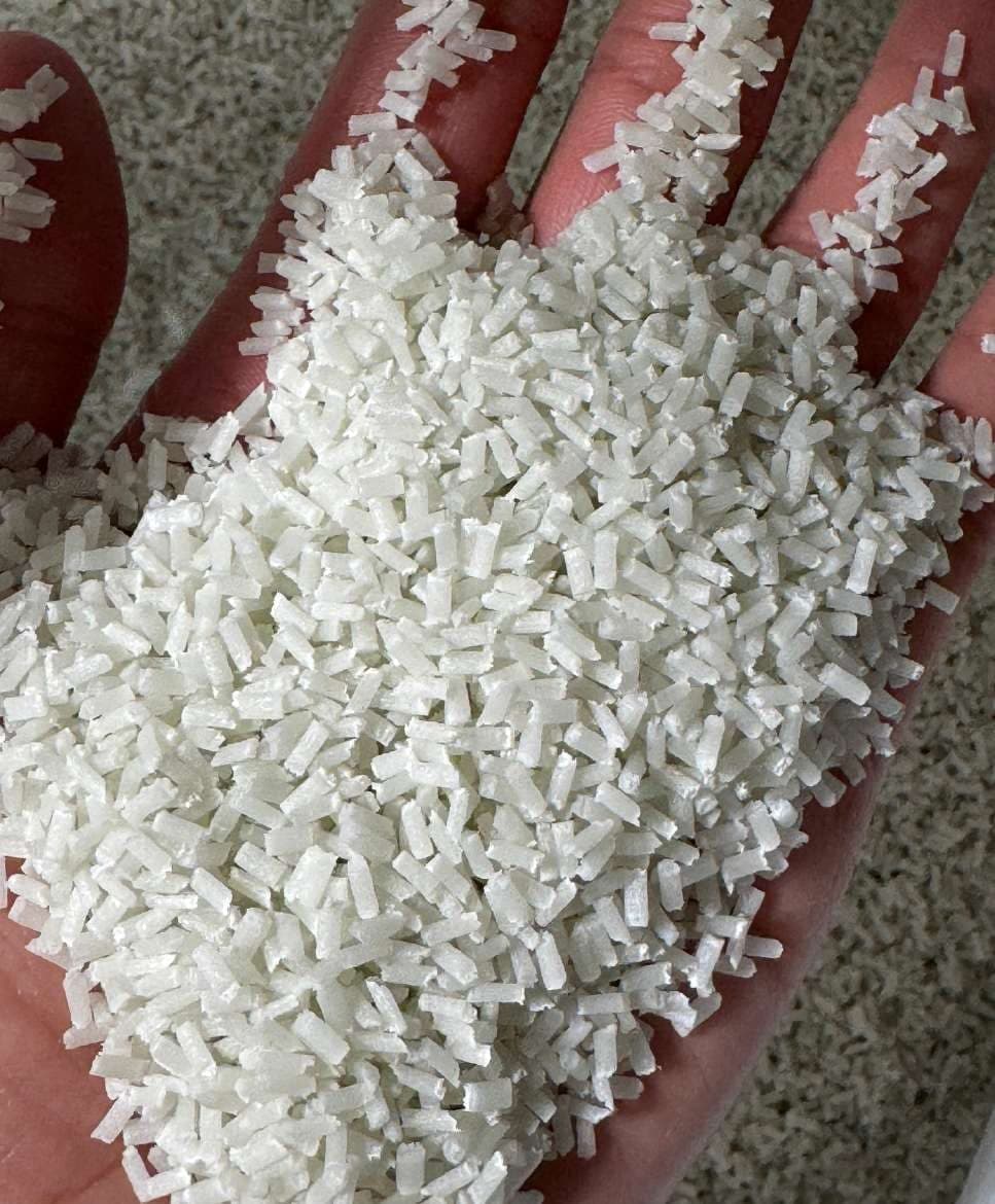 Elongated white glass-fiber compound pellets in the palm of a hand